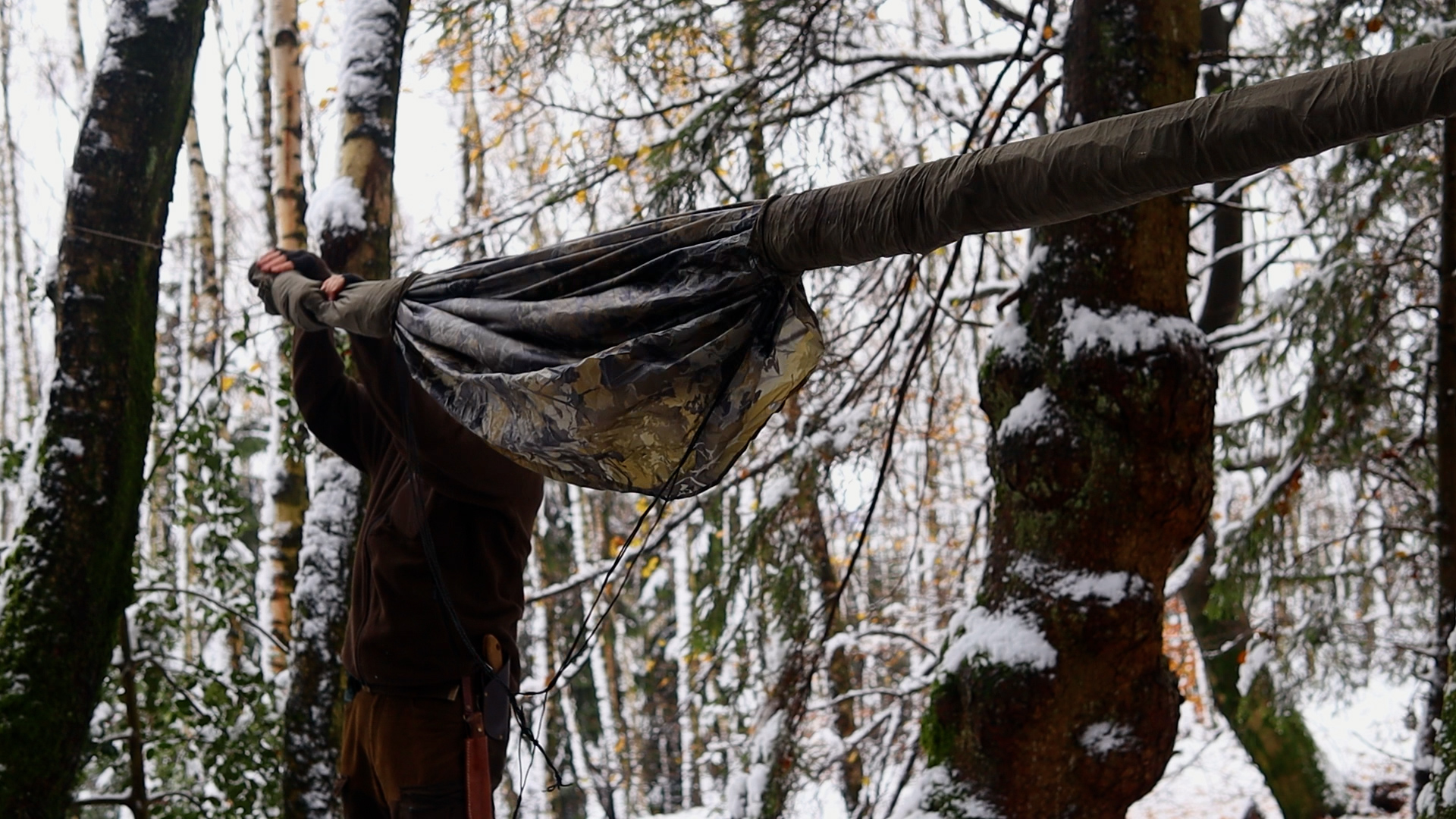 Hängematte wird im verschneiten Winterwald am Baum befestigt – Schlafplatz beim Winterbiwak