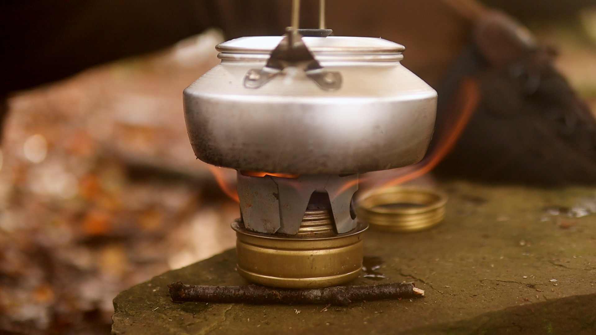 Nahaufnahme einer Trangia-Kanne über der blauen Flamme des Spiritus-Kochers – Morgenkaffee beim Winterbiwak