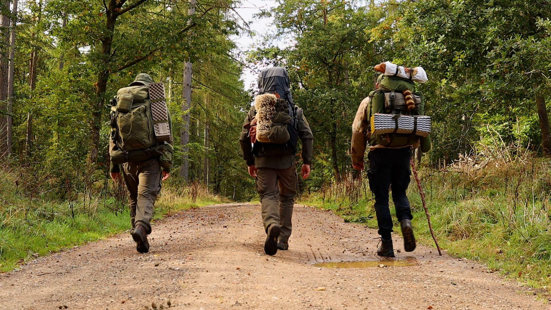 Drei Bushcrafter mit schweren Rucksäcken auf dem Weg zum Lagerplatz in der Hocheifel