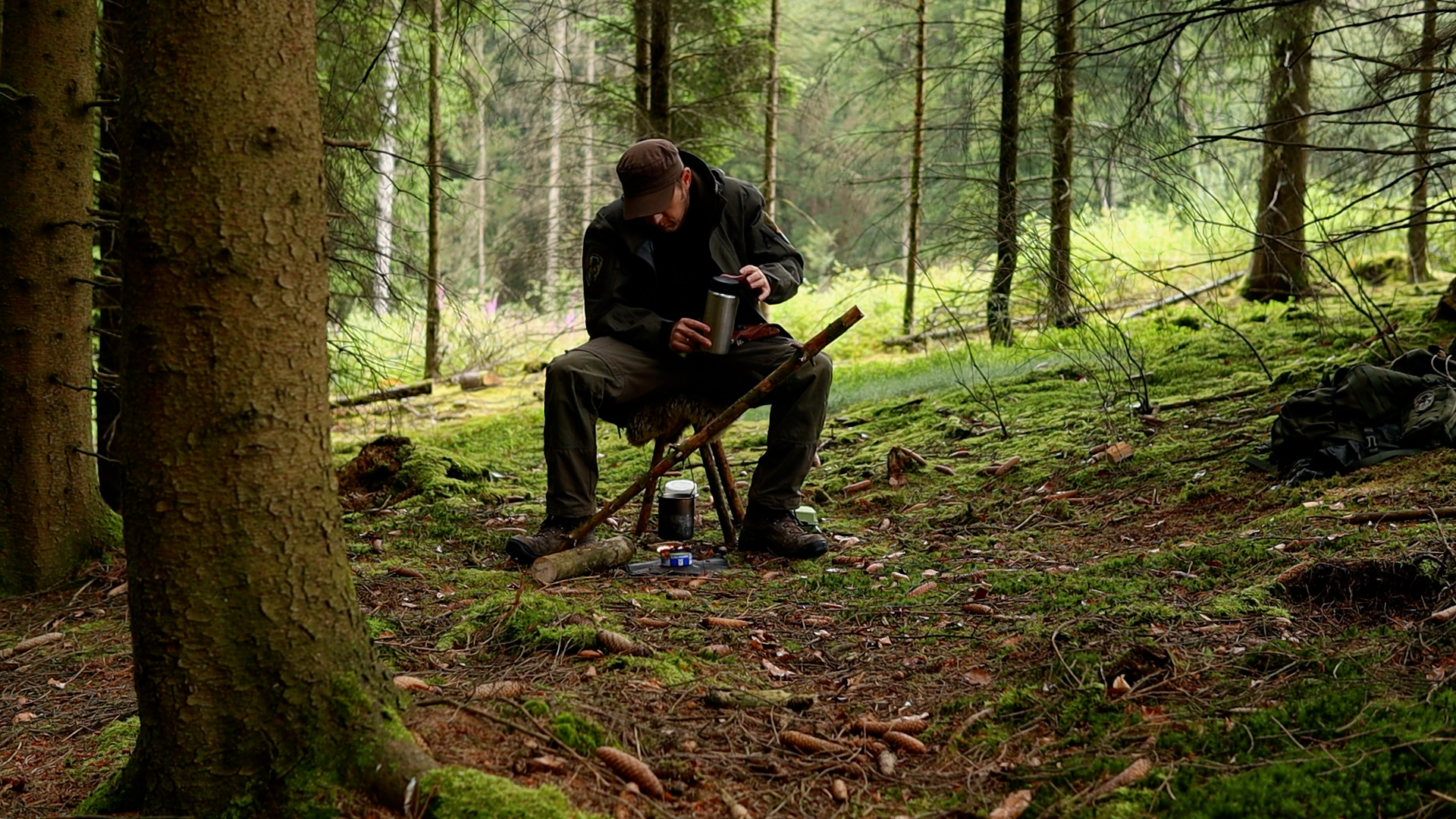 Simon sitzt auf dem fertigen Bushcraft-Dreibein-Hocker im Wald