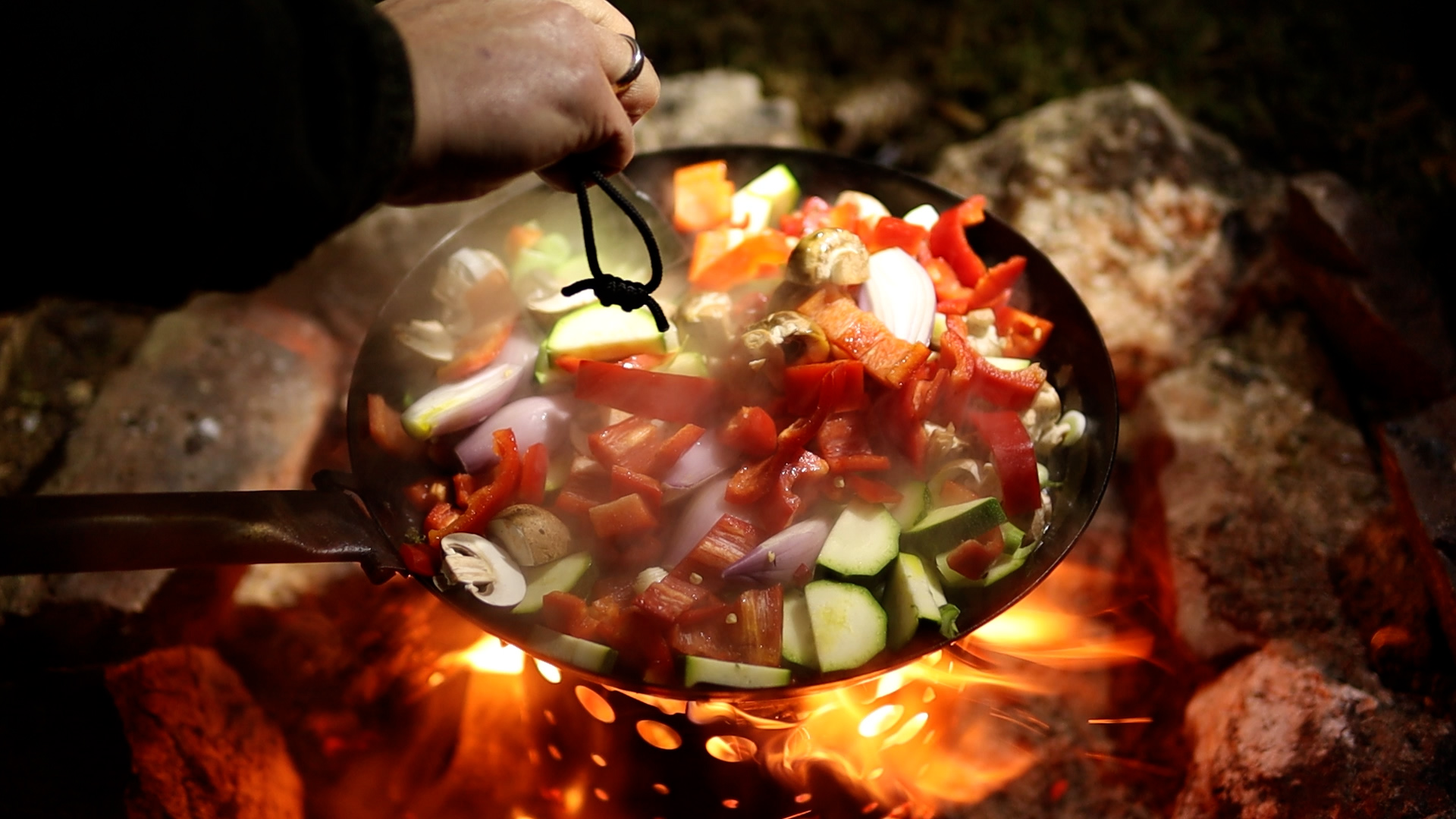 Frisches Gemüse in der Pfanne über offenem Lagerfeuer beim Bushcraft-Kochen