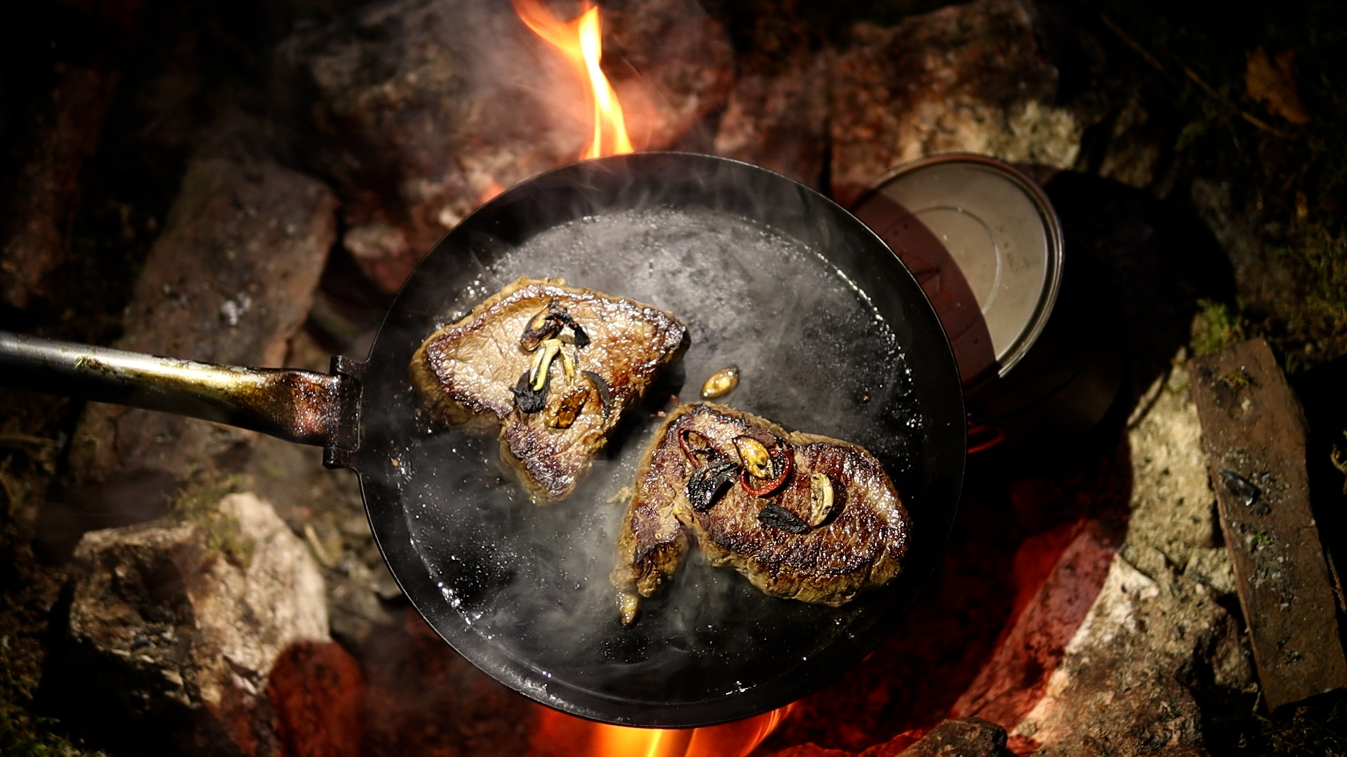 Steaks mit Knoblauch in der Pfanne über Lagerfeuerglut braten