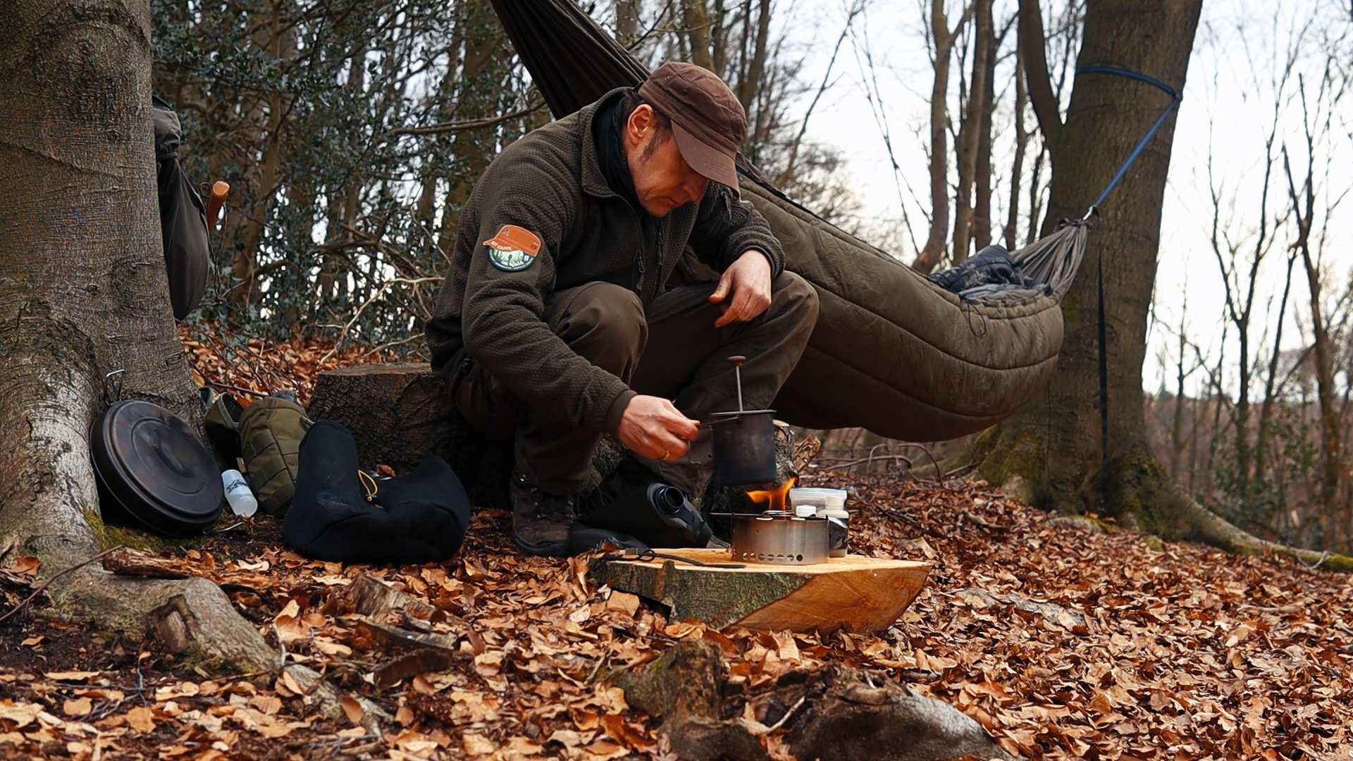 Simon kocht Morgenkaffee mit der French Press am Kocher, im Hintergrund hängt die onewind Hängematte mit Underquilt