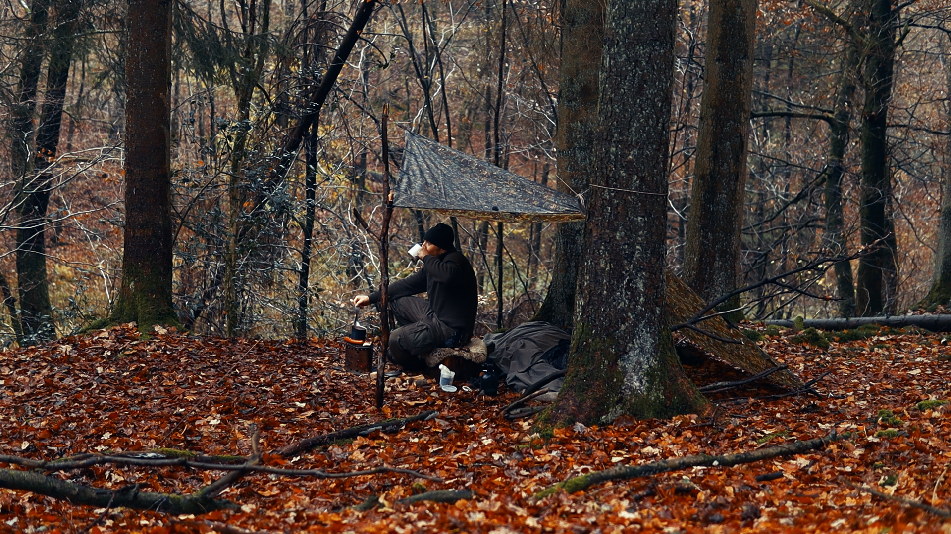 Simon Hilke trinkt Kaffee unter dem DD Tarp im herbstlichen Wald