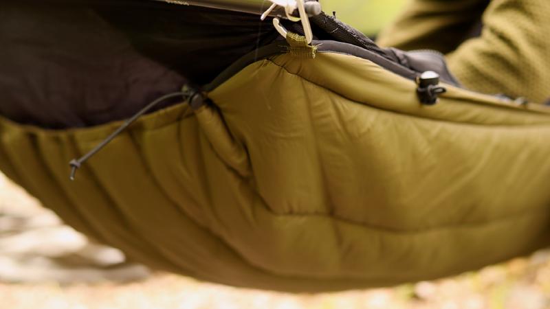 Nahaufnahme eines olivgrünen Underquilts, mit Karabiner unter der Hängematte eingehängt