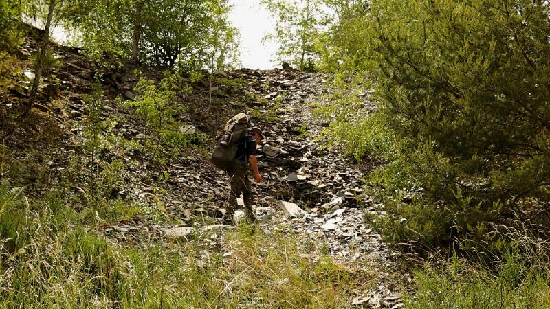 Person mit Rucksack steigt eine Halde aus Schiefergeröll hinauf