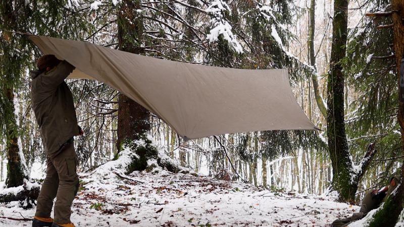Das Tarp wird zwischen den Bäumen im Winterwald aufgespannt